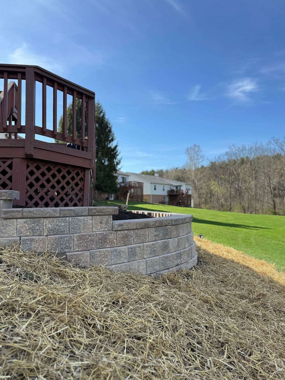 Wooden deck with stone steps leading to a green yard and residential buildings in the background.