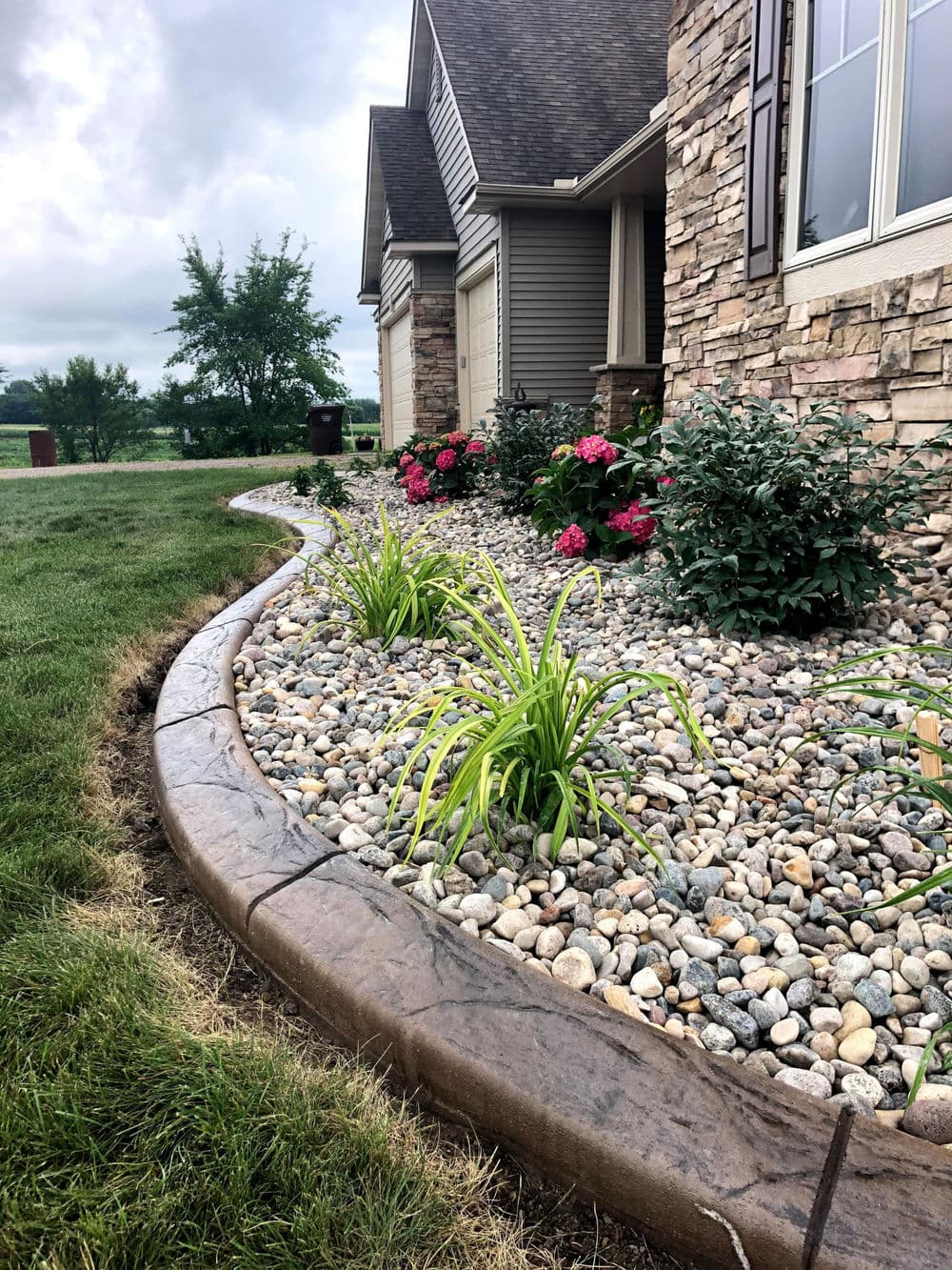 Landscaped garden featuring stone border, colorful flowers, and gravel ground cover.