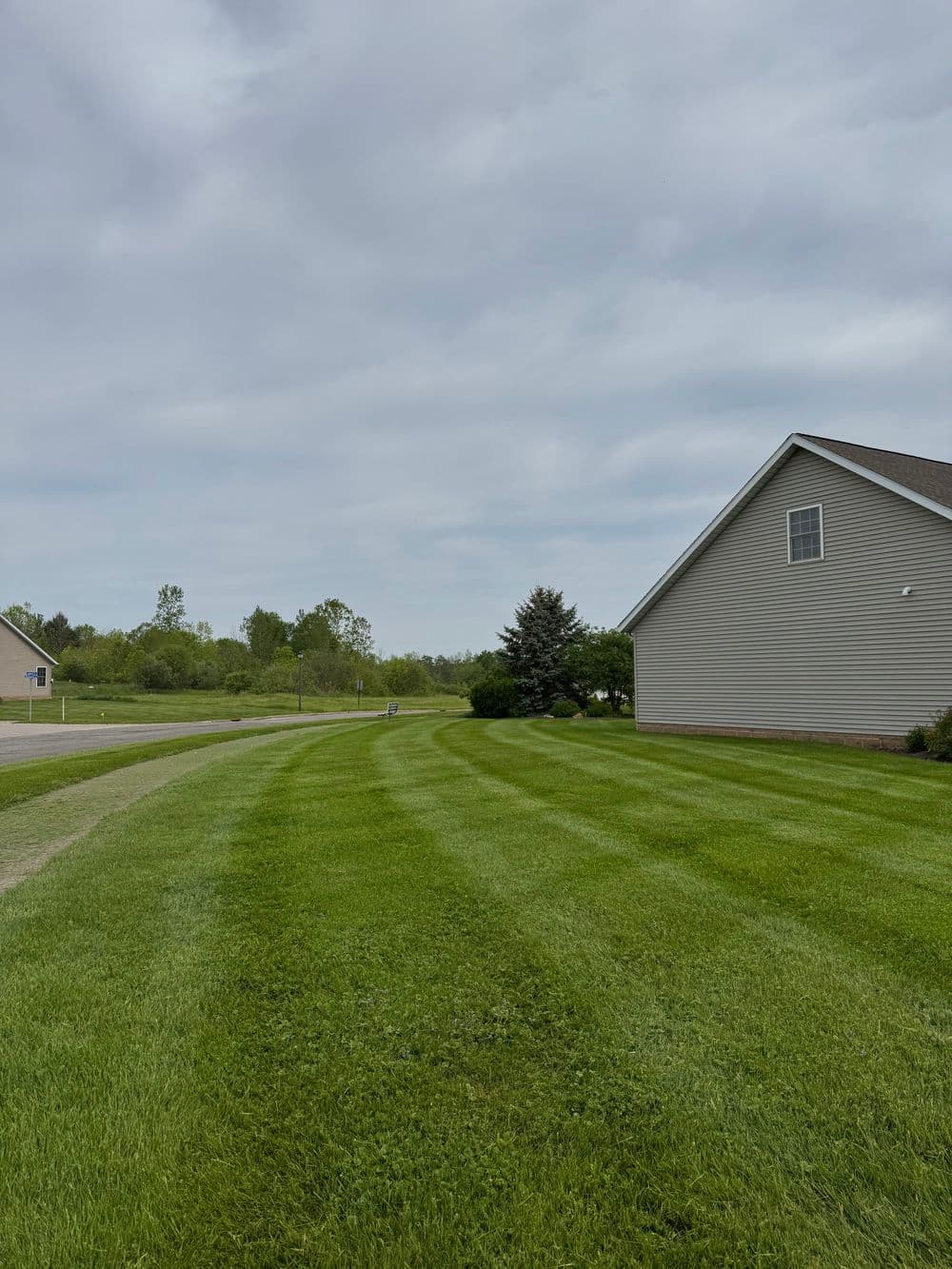 Lawn with neatly striped grass beside a residential house and cloudy sky.