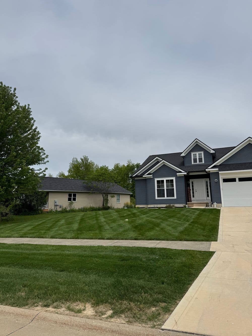 Modern blue house with landscaped lawn, driveway, and cloudy sky in the background.