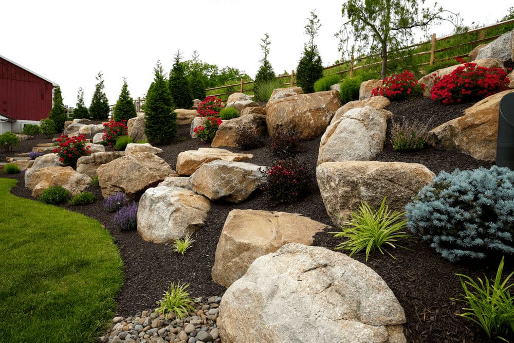 Landscaped garden featuring large rocks, colorful flowers, and lush greenery on a hill.
