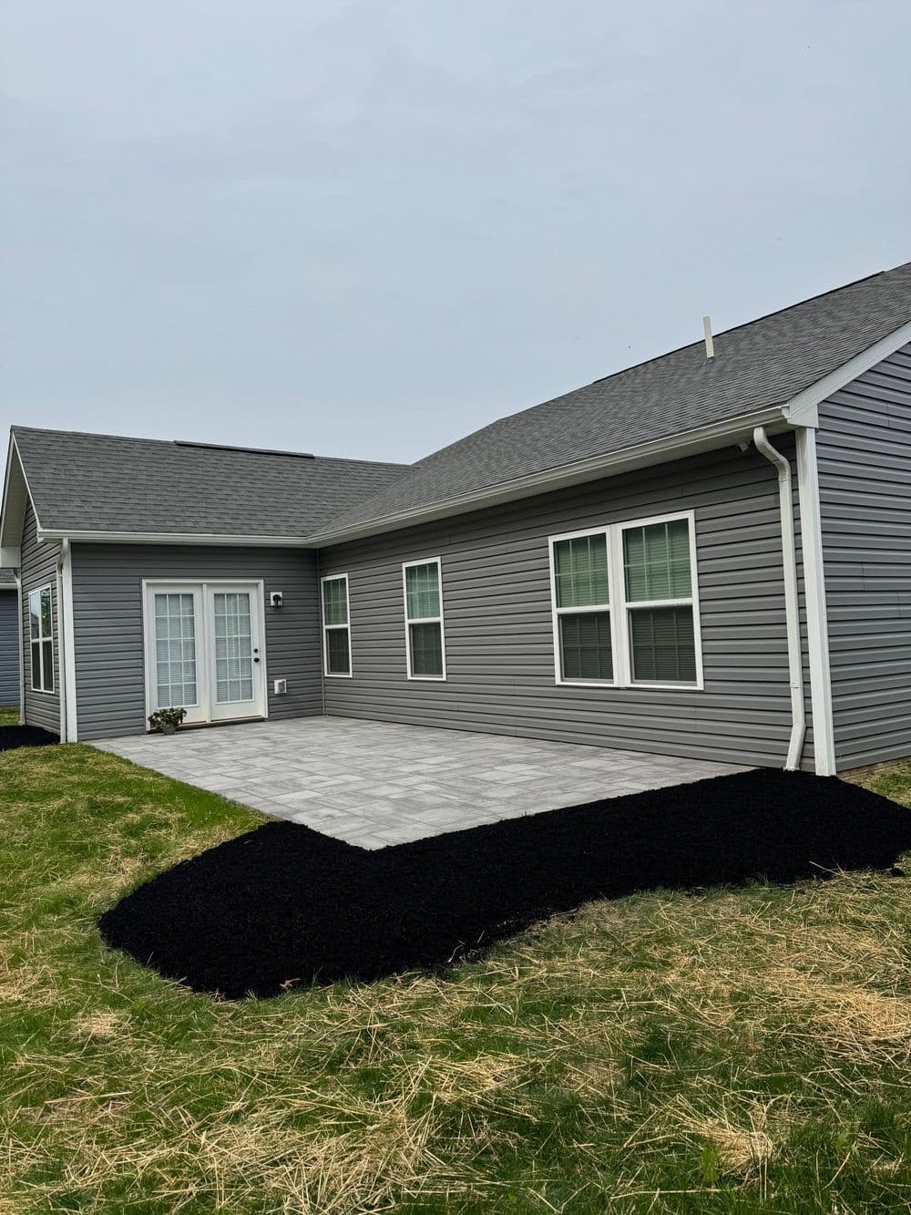 Modern gray house with a patio, surrounded by black mulch and grassy lawn.
