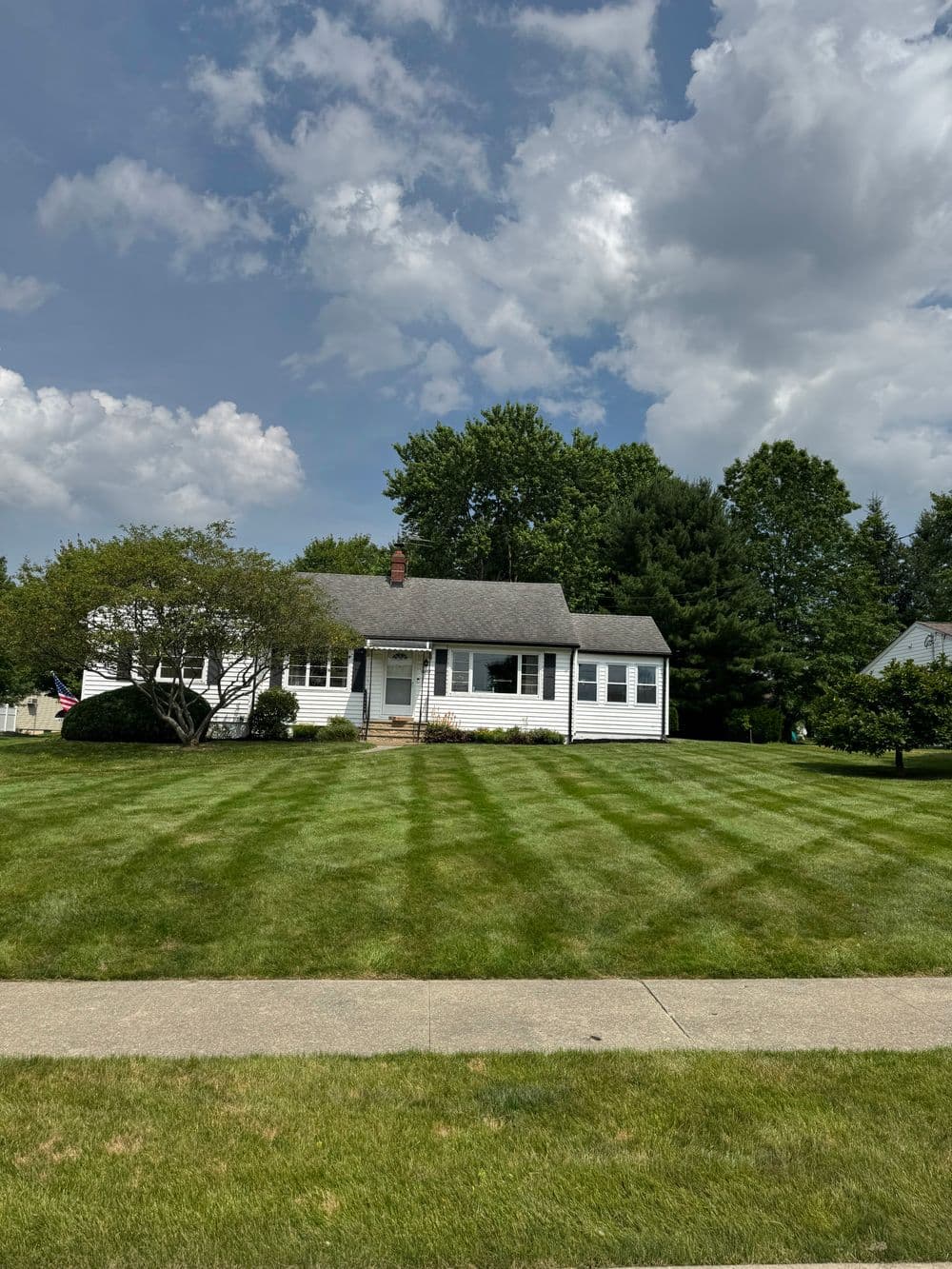 Charming white bungalow with manicured lawn and American flag under a cloudy sky.