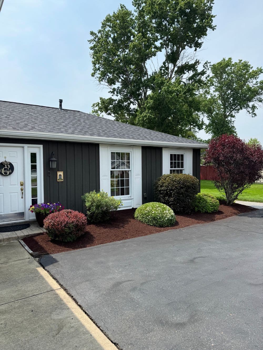 Charming gray house with landscaped garden and fresh mulch in front yard on a sunny day.