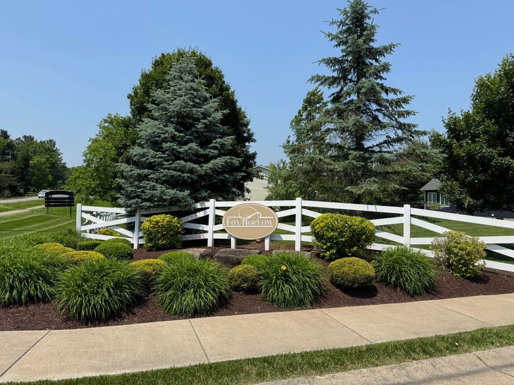 Scenic entrance of Fox Plantation with green landscaping and white fence on a sunny day.