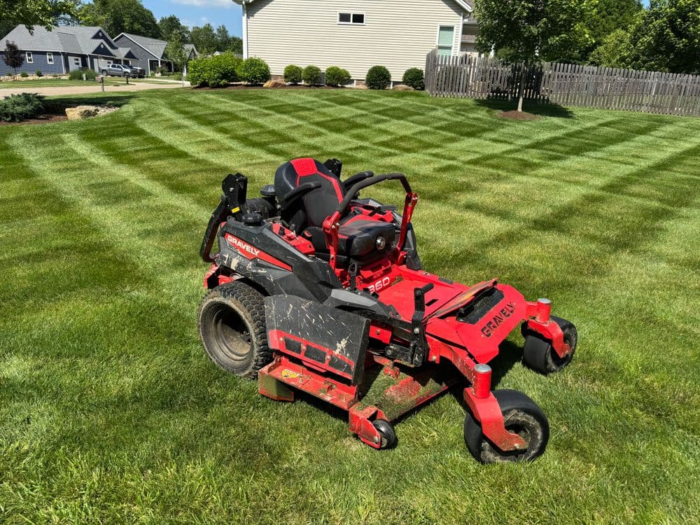 Red zero-turn lawn mower on freshly mowed grass with striped pattern in a residential yard.