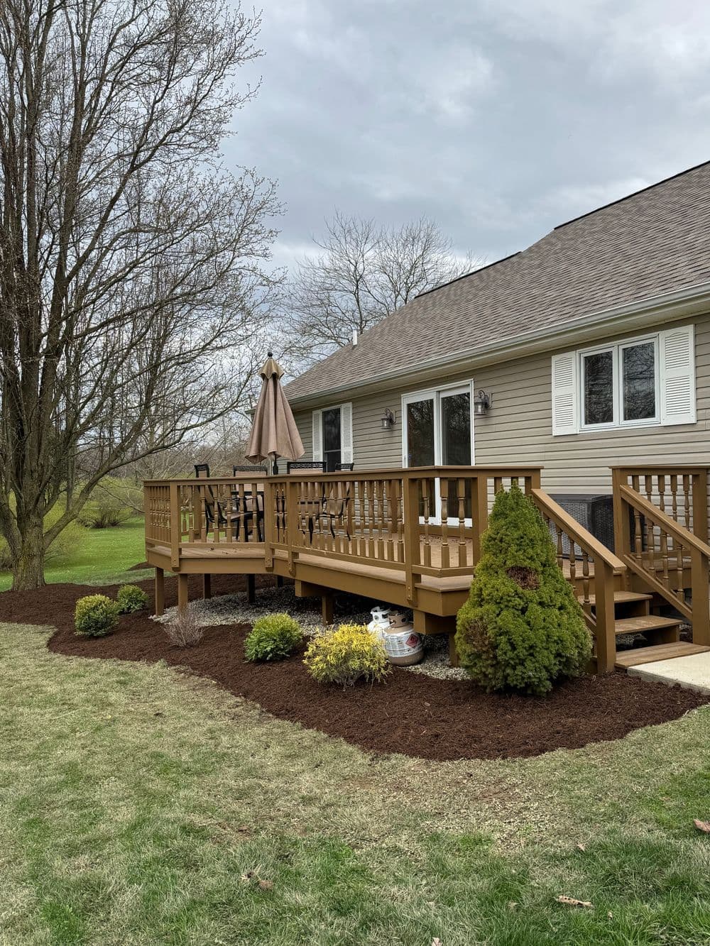 Modern wooden deck with patio furniture, surrounded by landscaped garden and trees.