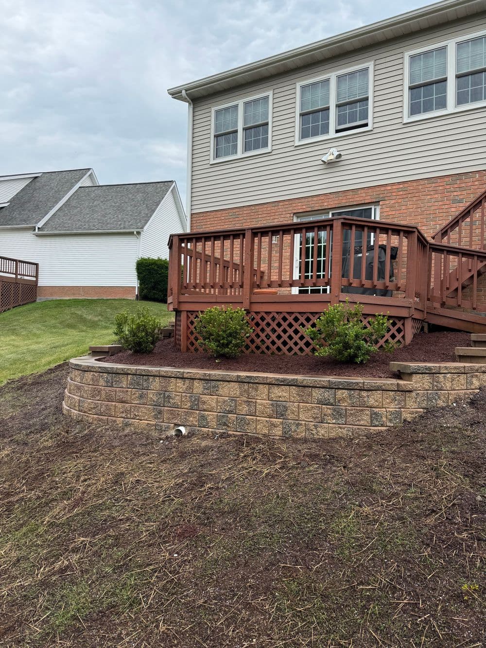 Wooden deck and landscaped garden with stone retaining wall beside a house.