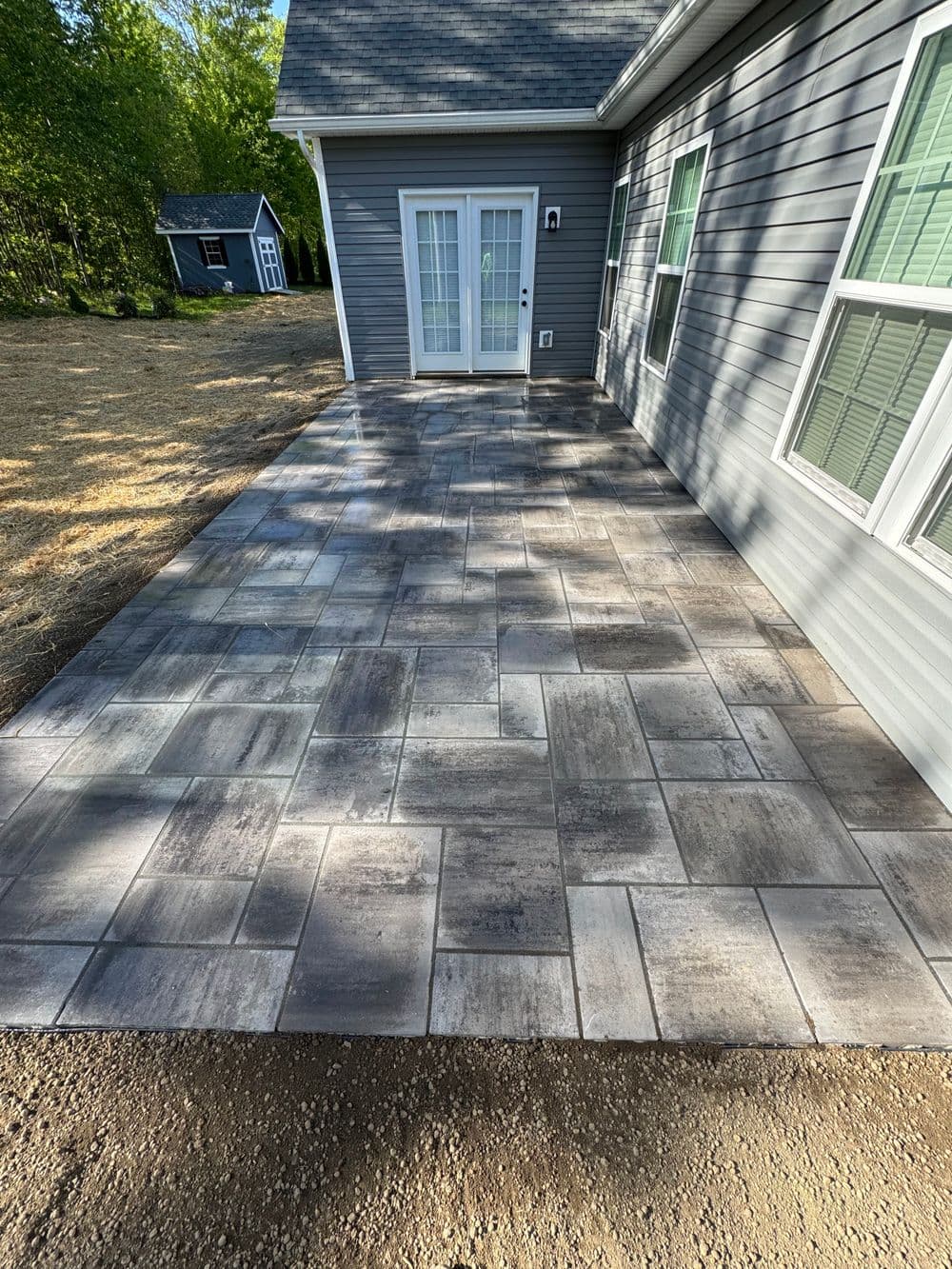 Newly installed gray textured patio tiles beside a house with large glass doors.