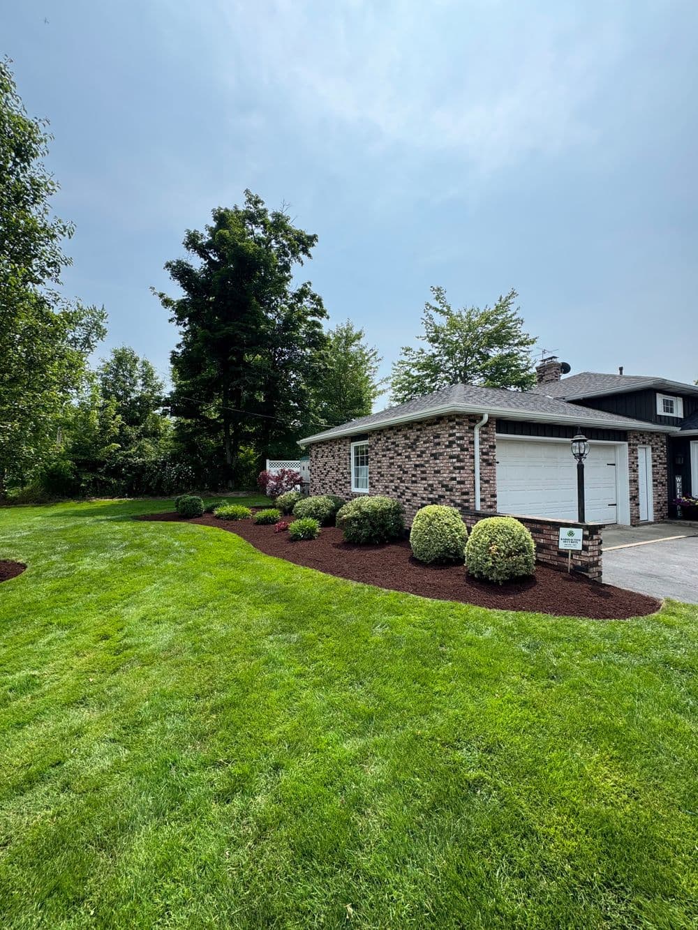 Brick house with manicured lawn and shrubs under cloudy sky. Outdoor landscaping features.