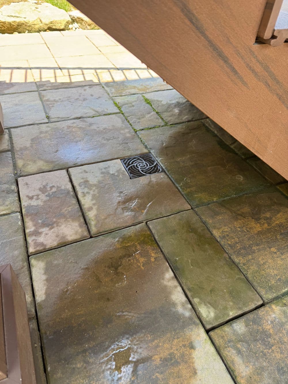 Drainage system on a stone patio with wet paving stones under a wooden deck.
