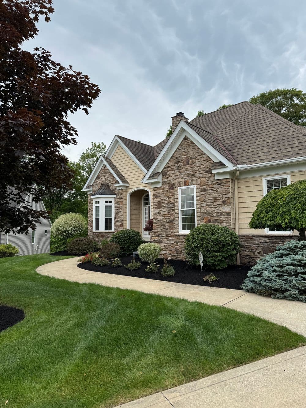 Charming stone and siding home with landscaped front yard and cloudy sky backdrop.