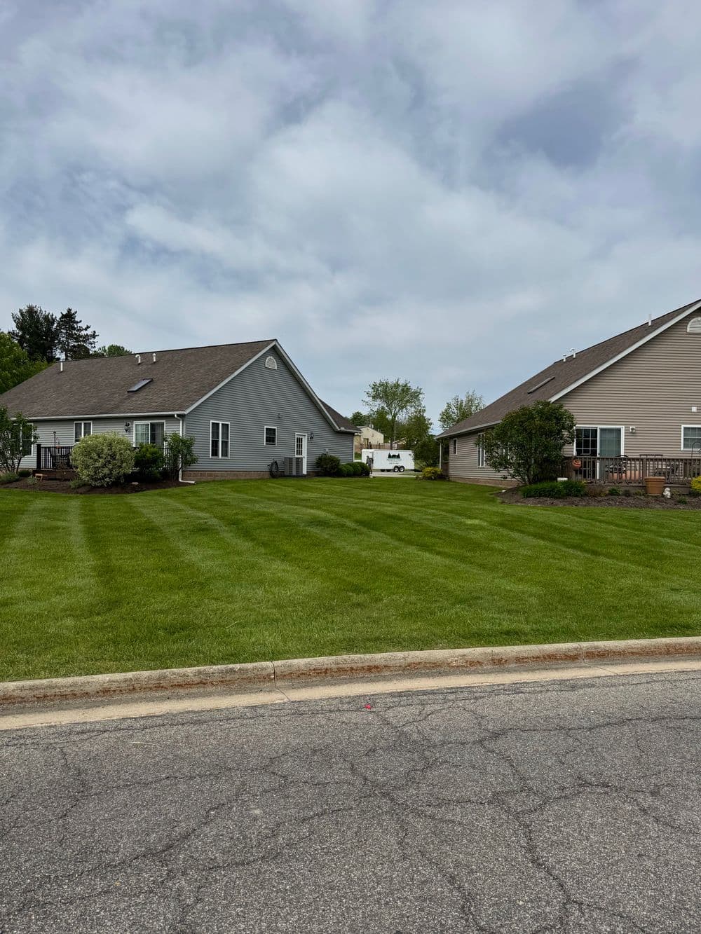 Two suburban homes with manicured lawns and cloudy skies in the background.