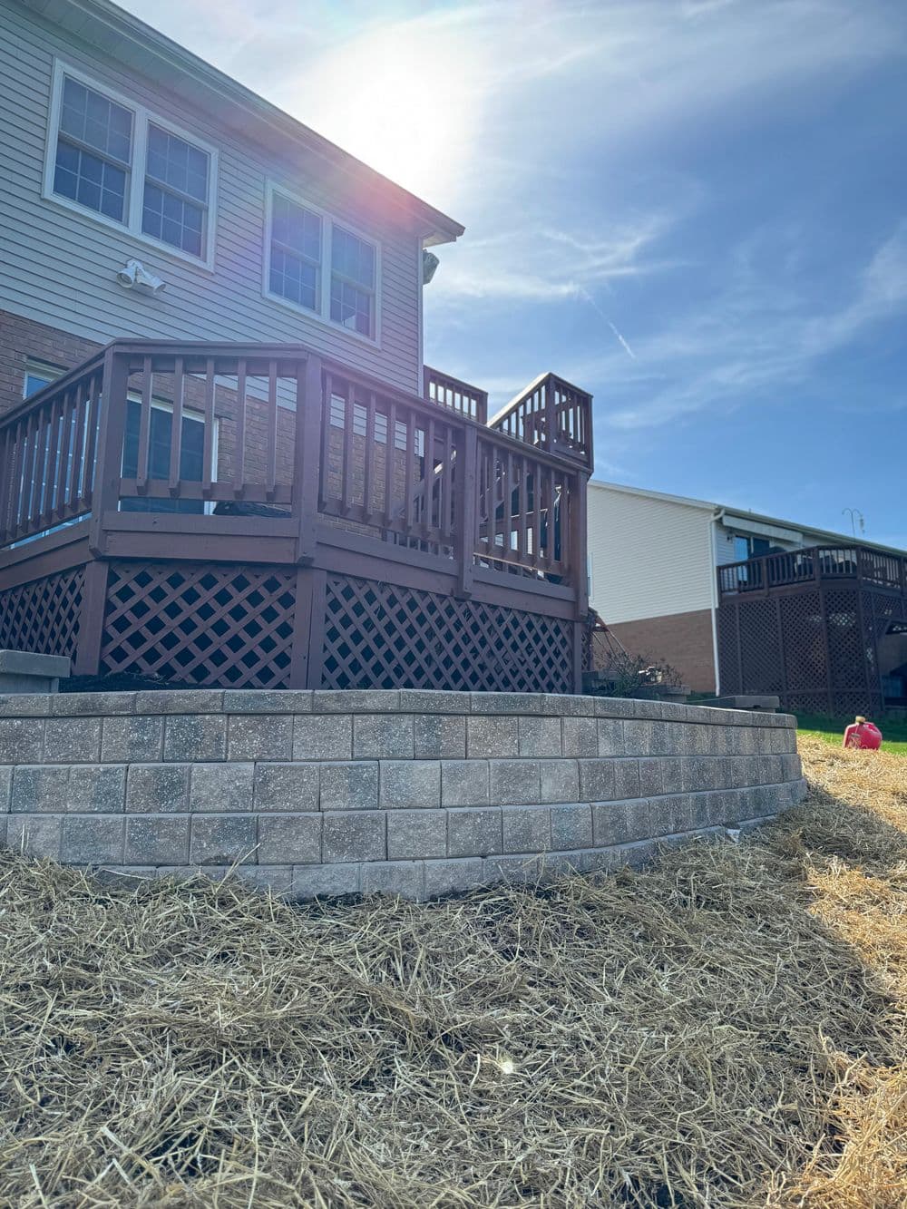 Sunny backyard with a wooden deck and stone wall garden edging.