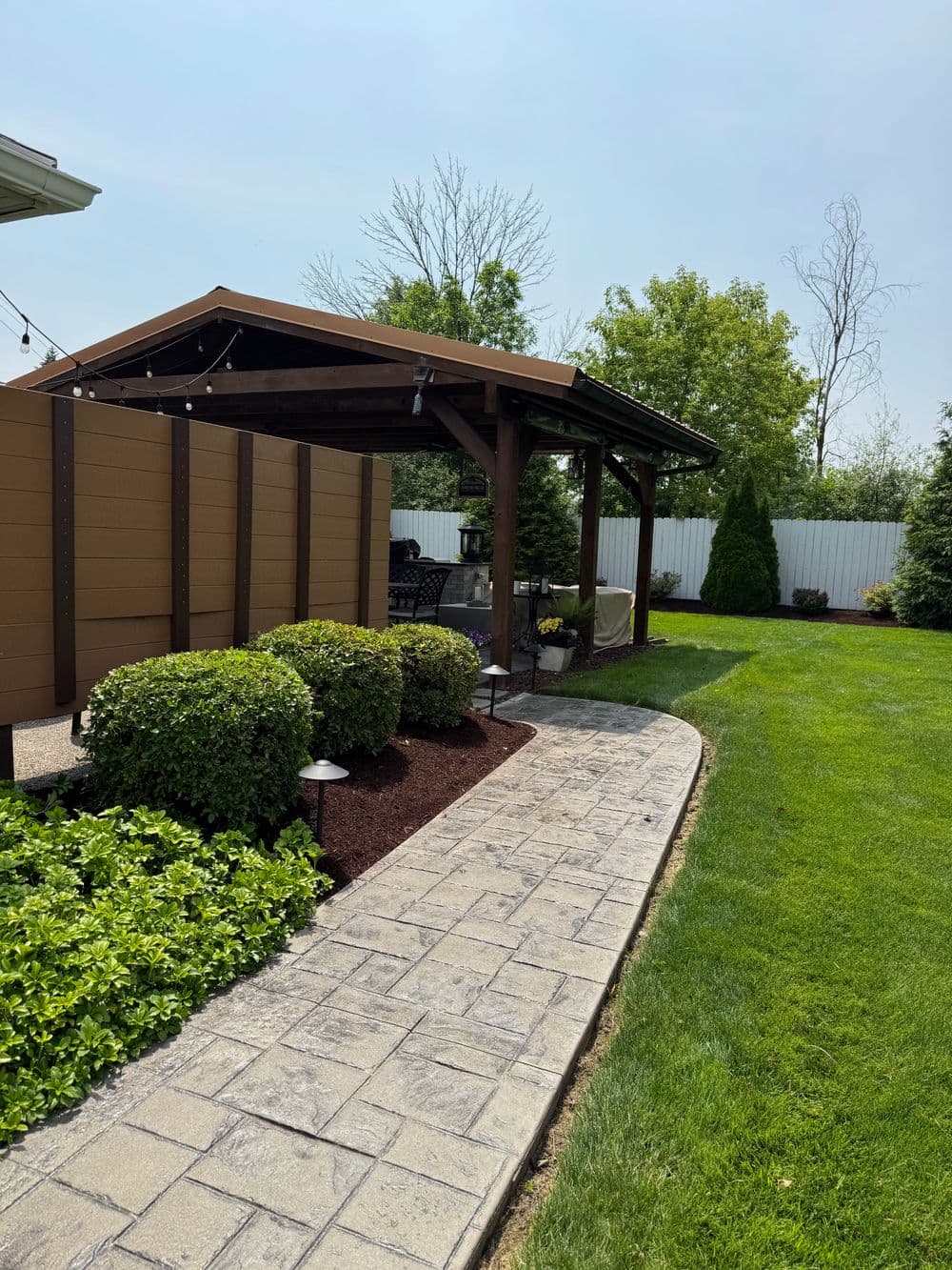 Backyard patio with shaded pavilion, landscaped path, and vibrant green lawn.