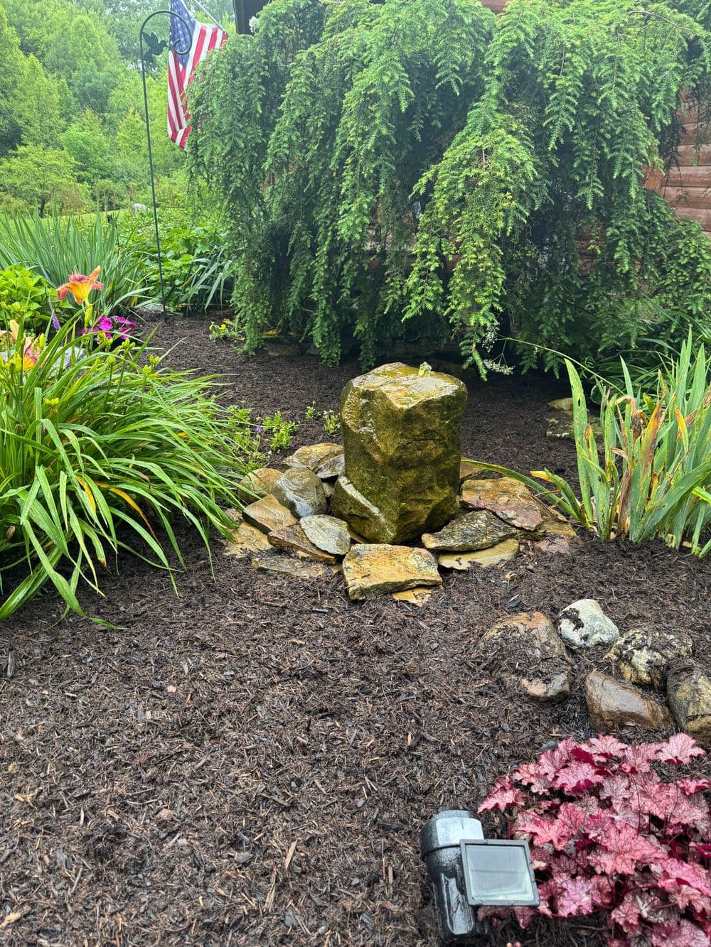 Stone feature surrounded by lush greenery and colorful flowers in a landscaped garden.