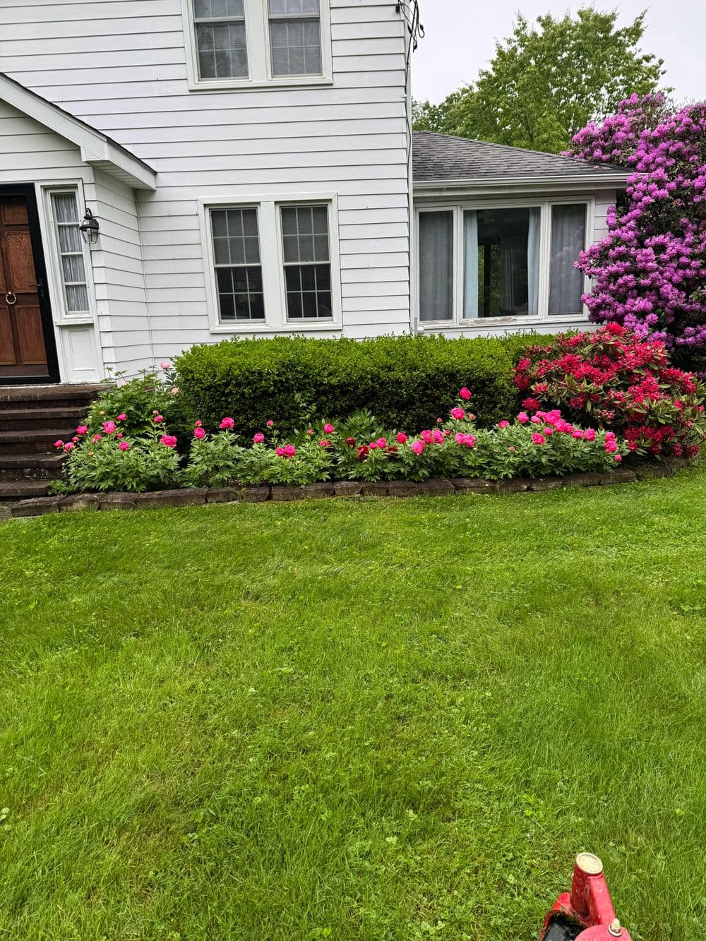 Colorful garden with pink flowers and lush greenery beside a white house.