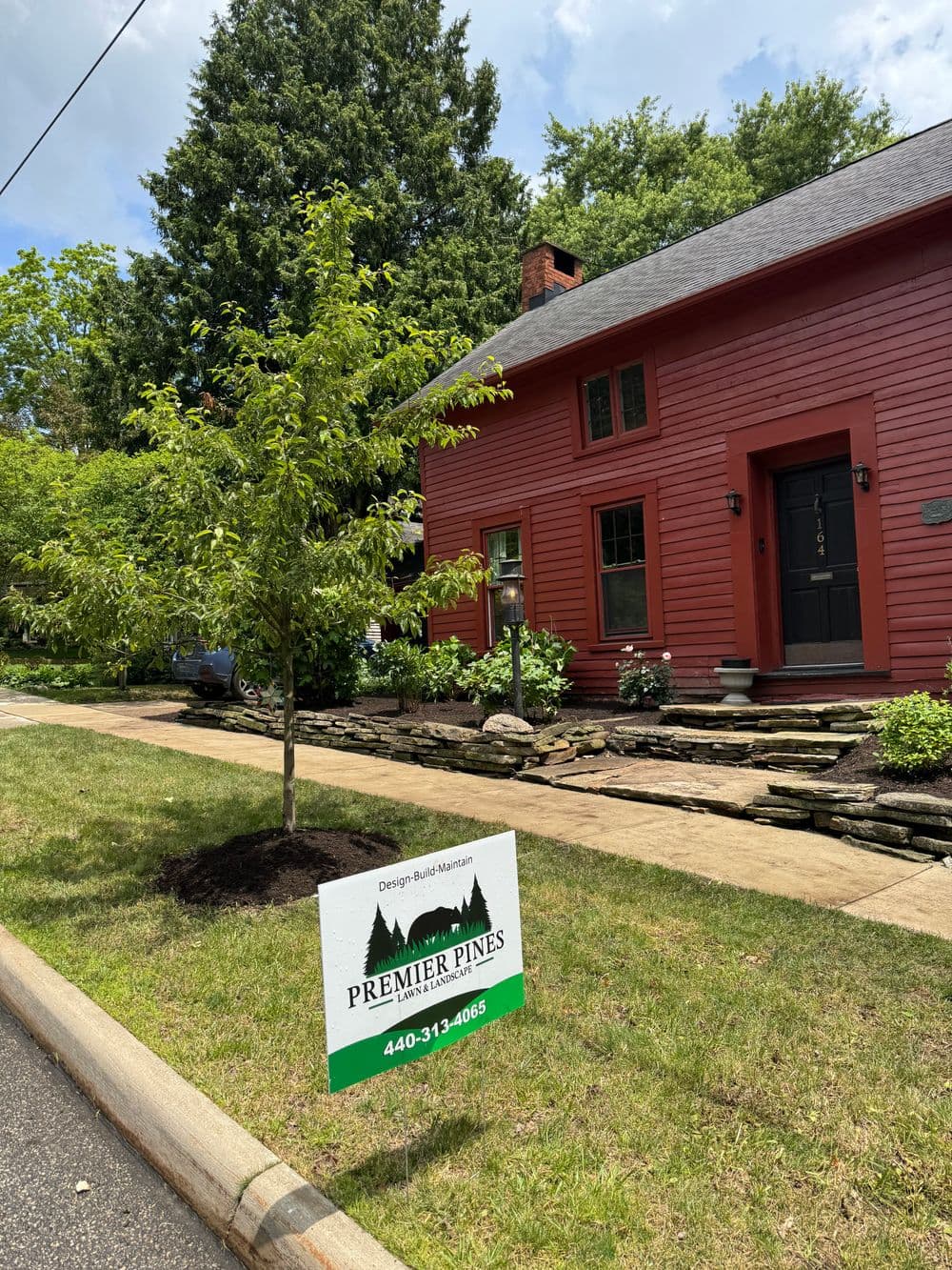 Red house with landscaped yard and Premier Pines sign, showcasing home design services.