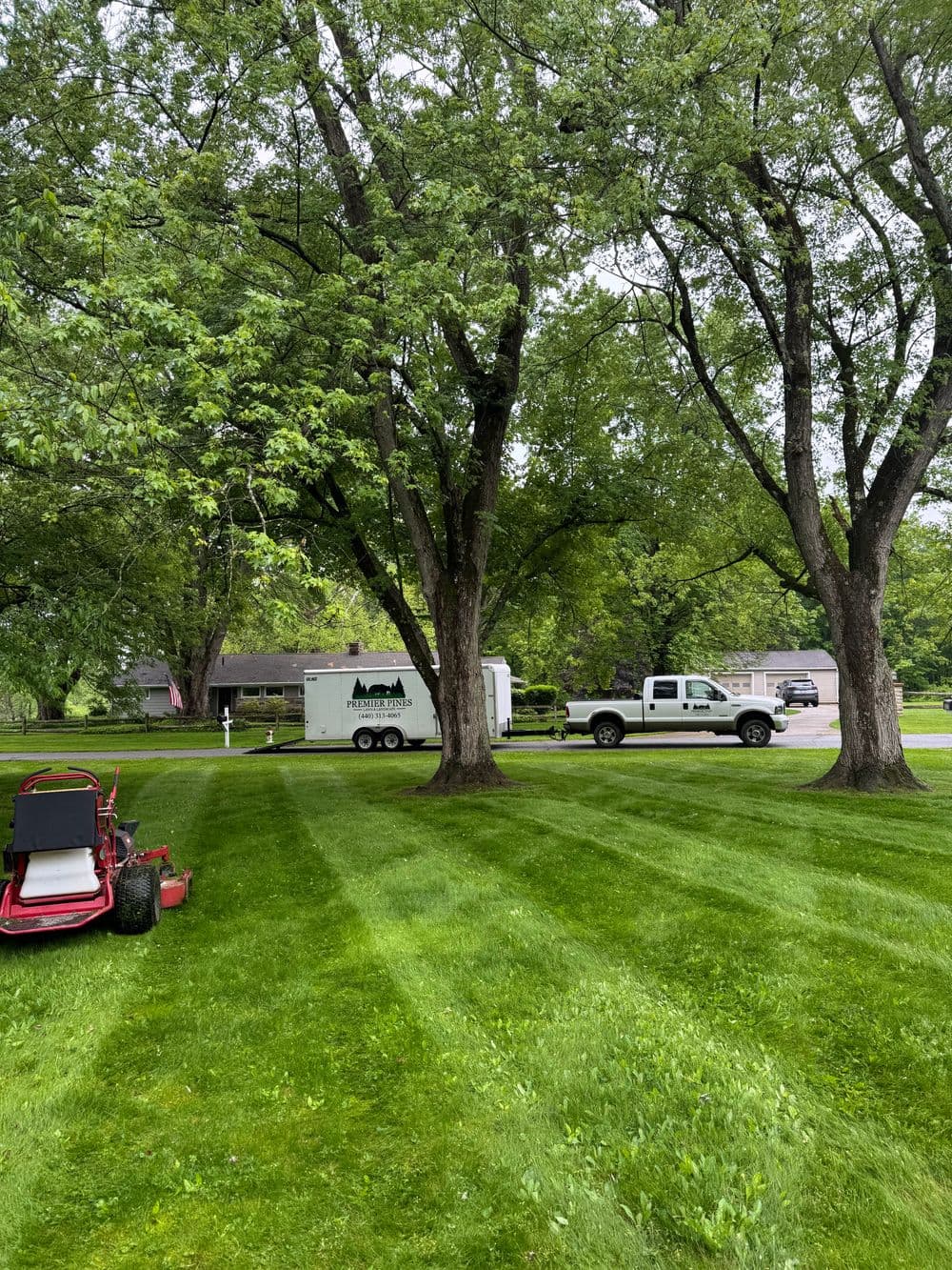 Lawn care scene featuring a parked truck and trailer under lush green trees.