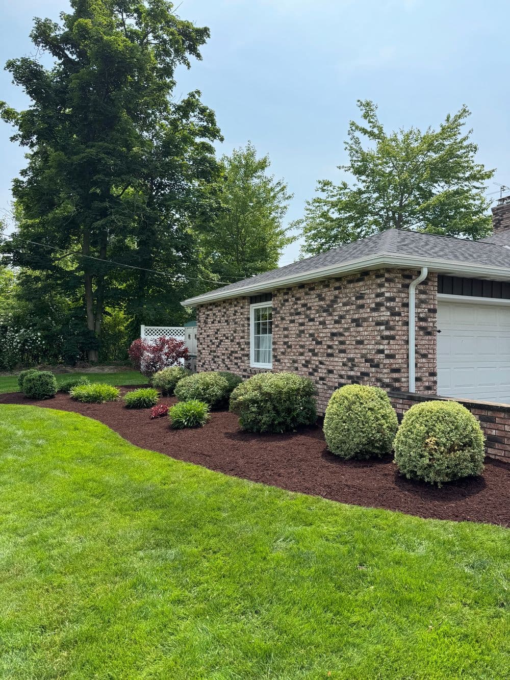 Well-maintained brick house with landscaped garden and fresh mulch in sunny yard.