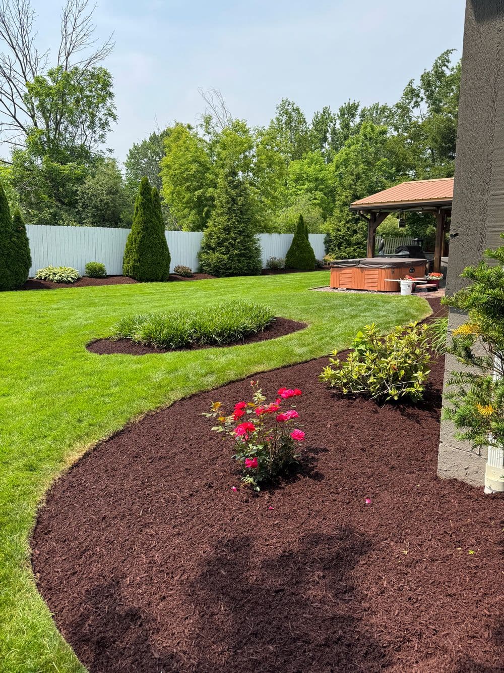 Lush backyard with manicured lawn, flower beds, and a hot tub under a gazebo.